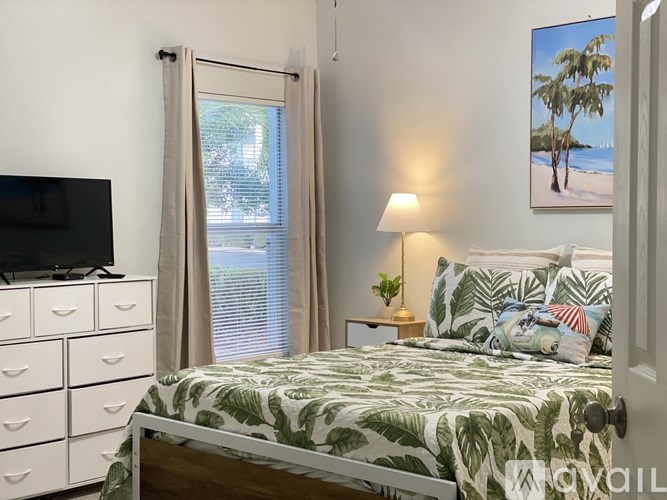 A bedroom with a bed, nightstand, and a painting of a beach scene on the wall.