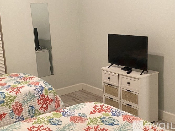 A bed with a floral comforter sits next to a white cabinet with a television on top.