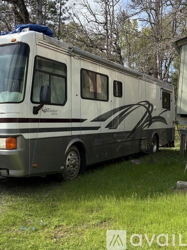 A white RV with a black stripe and the word "Williams" written on it is parked in a grassy area.