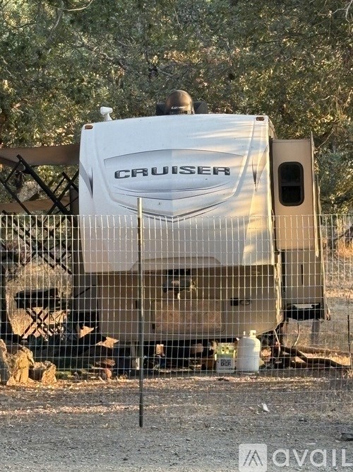 A white Cruiser RV is parked behind a wire fence.