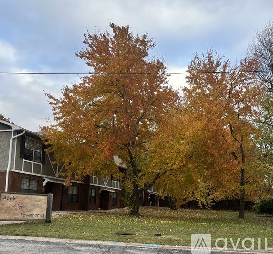 A tree with orange leaves stands in front of a building with a sign that reads "Apple Glen Townhomes".