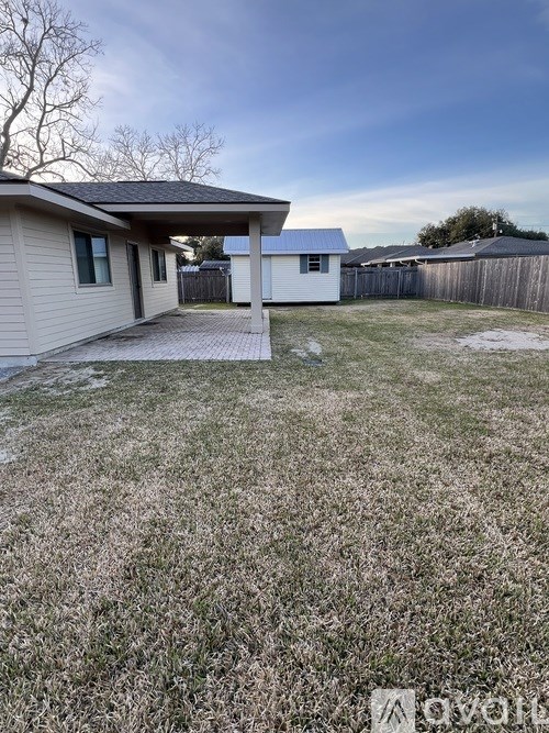 A house with a covered patio is surrounded by a fence and a grassy yard.