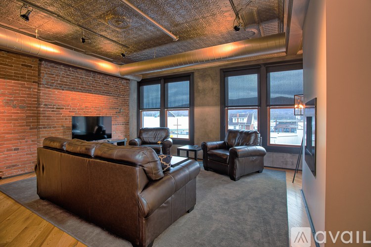 A living room with a brown leather couch and a brick wall.
