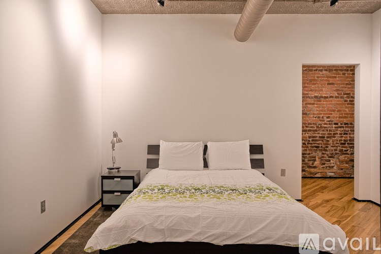 A bedroom with a bed, nightstand, and a brick wall.