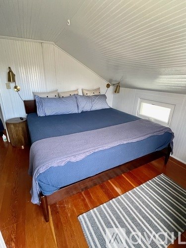 A bed with a blue blanket and pillows in a room with wooden floors.