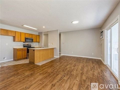 A spacious living room with wooden flooring and a kitchen area with wooden cabinets and appliances.