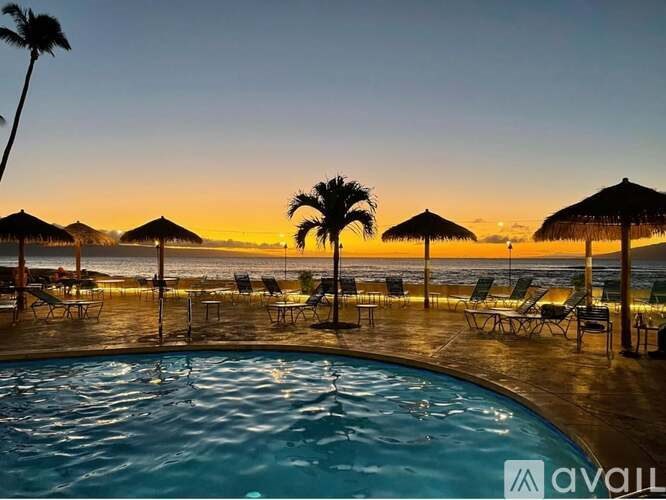 A pool area with sun loungers and palm trees at sunset.