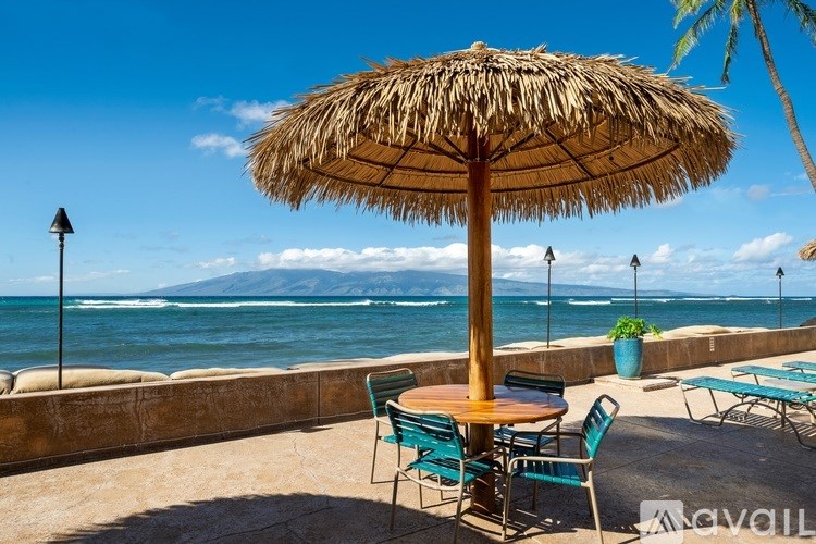 A straw umbrella shades a table with chairs on a patio overlooking the ocean.