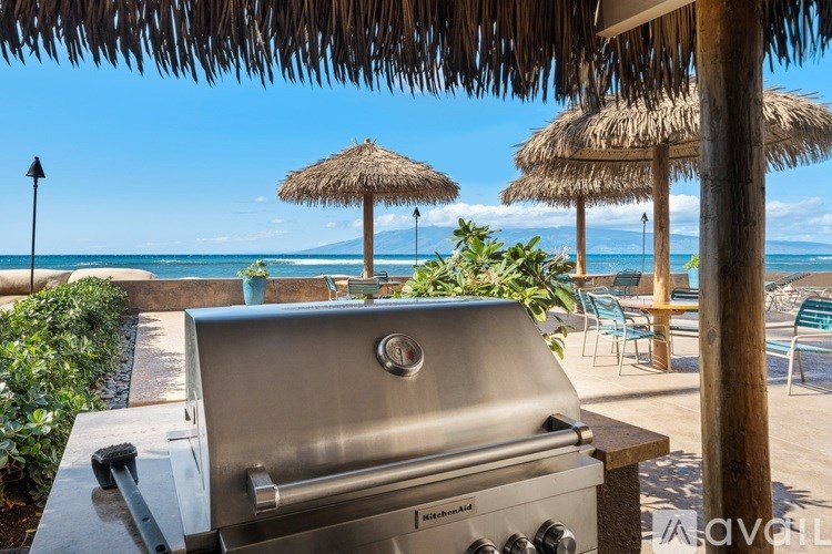 A stainless steel grill is in the foreground of a beachside patio.