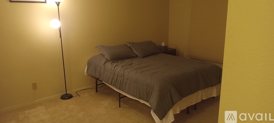 A bedroom with a bed, pillows, and a floor lamp.