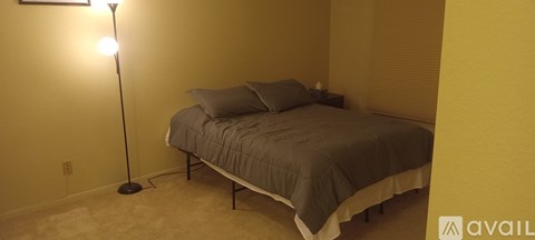 A bedroom with a bed, pillows, and a floor lamp.
