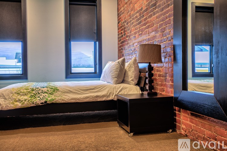 A bedroom with a bed, a lamp, and a brick wall.