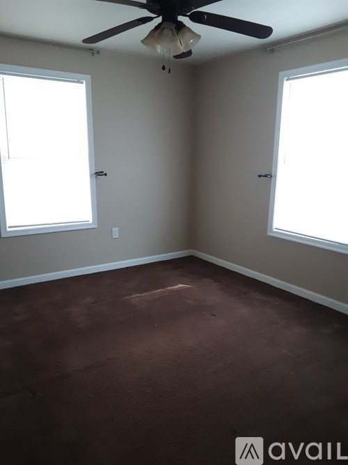 A room with a ceiling fan and two windows.