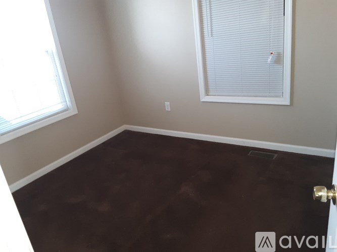A room with a brown floor and a window with blinds.