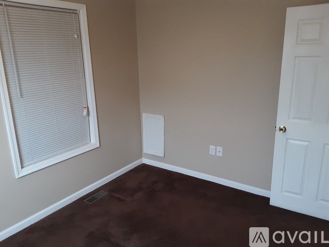 A room with a white door, window with blinds, and a wall socket.