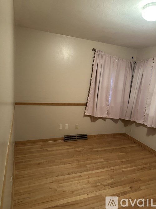 A room with wooden flooring and a window with curtains.