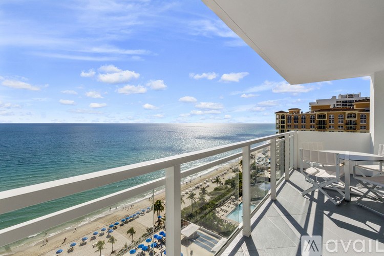 A balcony overlooks a beach with blue umbrellas and a building in the distance.