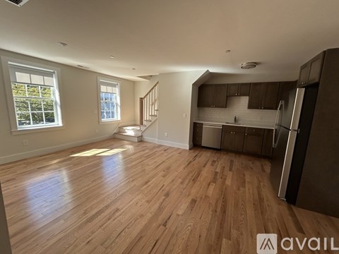 A spacious kitchen with wooden floors and a refrigerator on the right side.