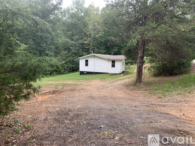 A small white house is situated in a wooded area with a dirt path leading to it.