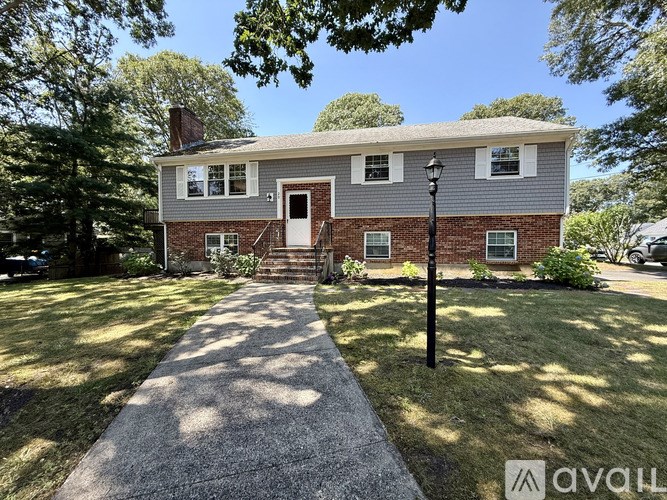 A house with a brick facade and a white roof is surrounded by greenery.