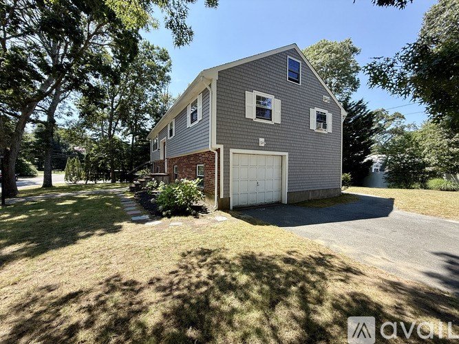 A house with a grey exterior and a white garage door is surrounded by trees.
