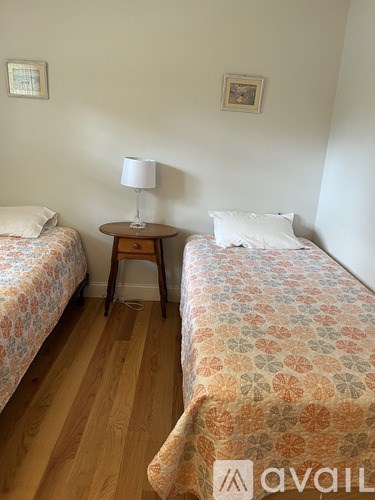 Two beds with floral patterns are in a room with wooden floors and white walls.