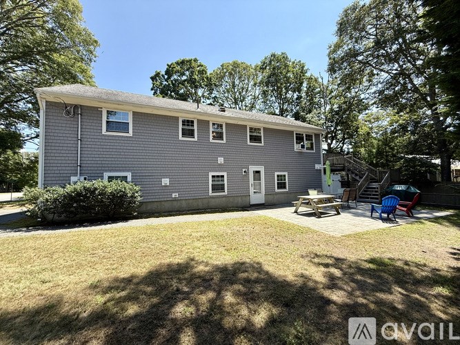 A grey house with a white door and windows, surrounded by a grassy area and trees.