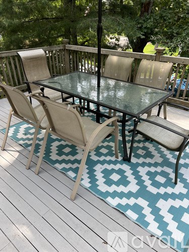 A glass table surrounded by chairs on a deck.