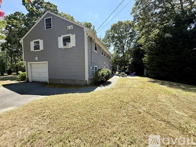 A grey house with a white garage door is surrounded by a grassy area and trees.