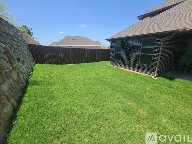 A backyard with a stone wall and a house with a brown roof.