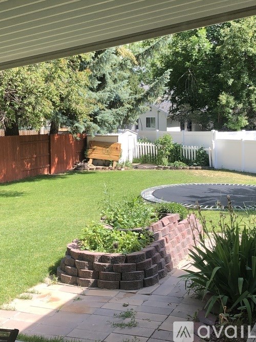 A backyard with a white picket fence and a circular brick planter.