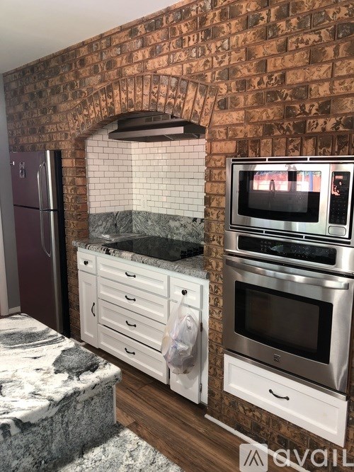 A kitchen with a brick wall and a microwave on top of the oven.