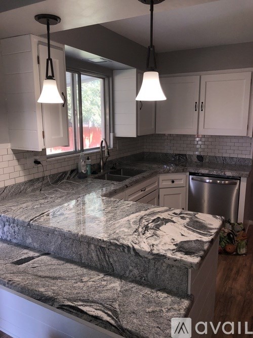 A kitchen with a granite countertop and pendant lights.