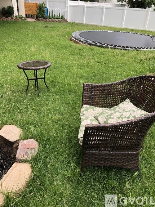 A brown wicker chair with a cushion is placed on a grassy lawn.