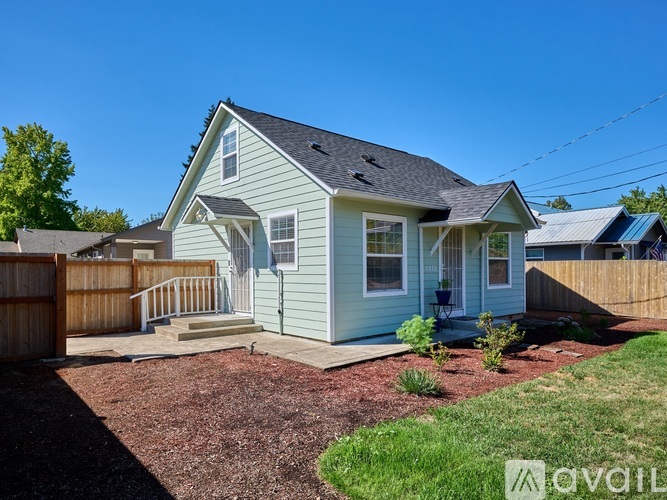 A house with a blue siding and a grey roof is surrounded by a wooden fence.