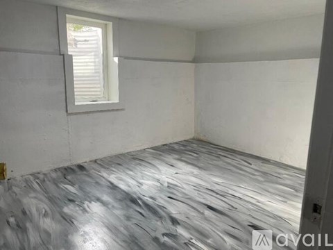 A room with a grey wooden floor and a window with blinds.