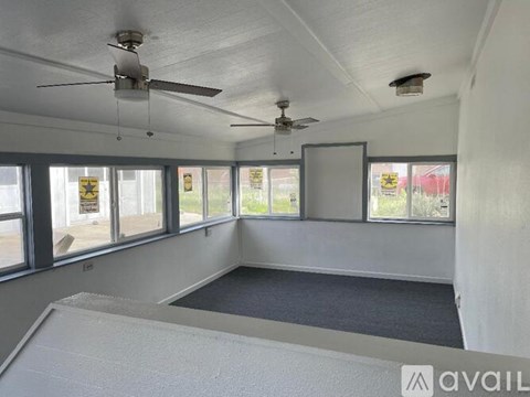 A room with a ceiling fan and large windows.