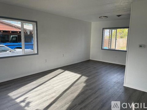 A room with wooden flooring and two windows.