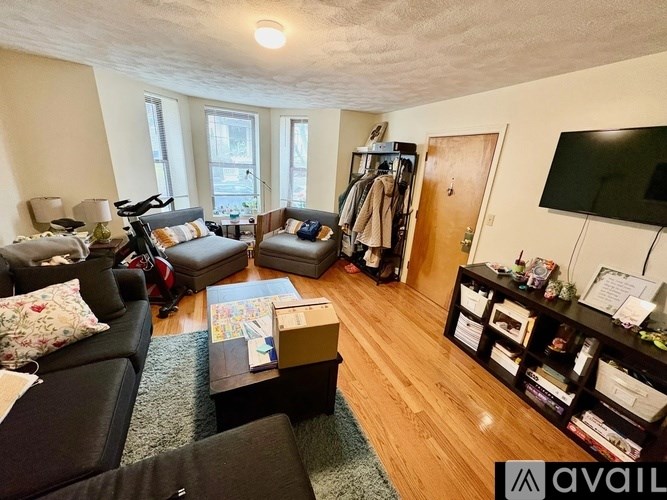A living room with a black couch, a coffee table, and a TV mounted on the wall.
