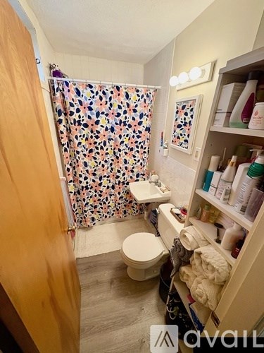 A small, well-stocked bathroom with a toilet, sink, and shower curtain.