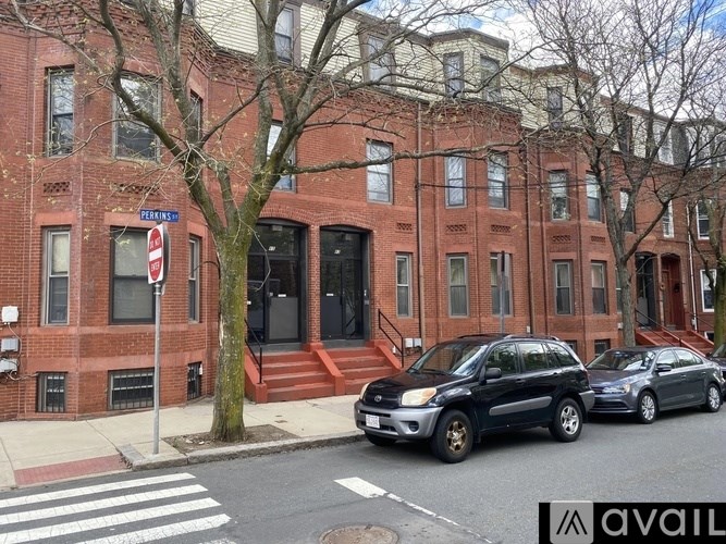 A street view of a red brick building with cars parked in front.