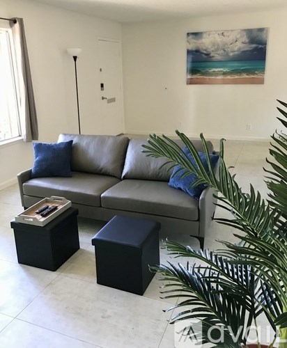 A living room with a grey couch, two black ottomans, and a plant.