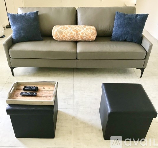A grey couch with a wooden tray on top of it and two black ottomans.