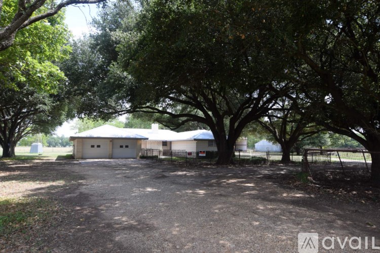 A gravel driveway leads to a white house with a metal fence.