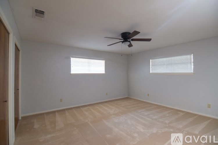 A room with a ceiling fan and two windows.