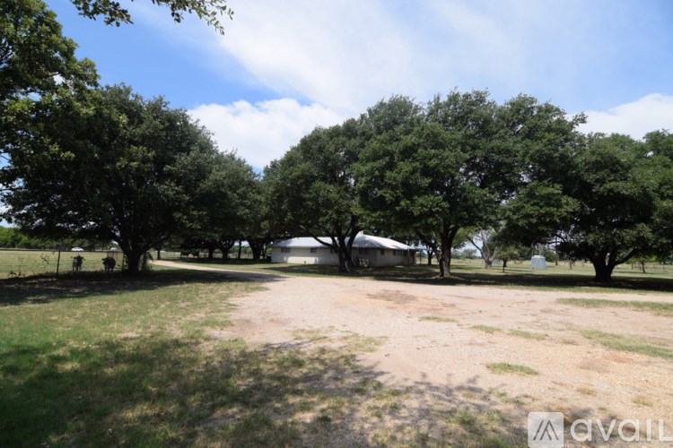 A grassy field with trees and a house in the background.