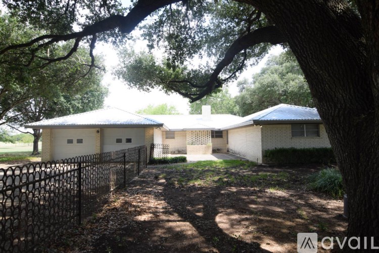 A house with a white exterior and a black fence is surrounded by trees.