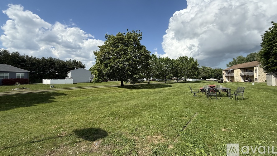 A large grassy field with a tree in the middle and a building in the background.