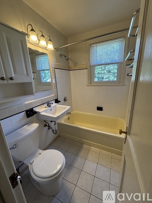 A white toilet is in a bathroom with a white tub and sink.
