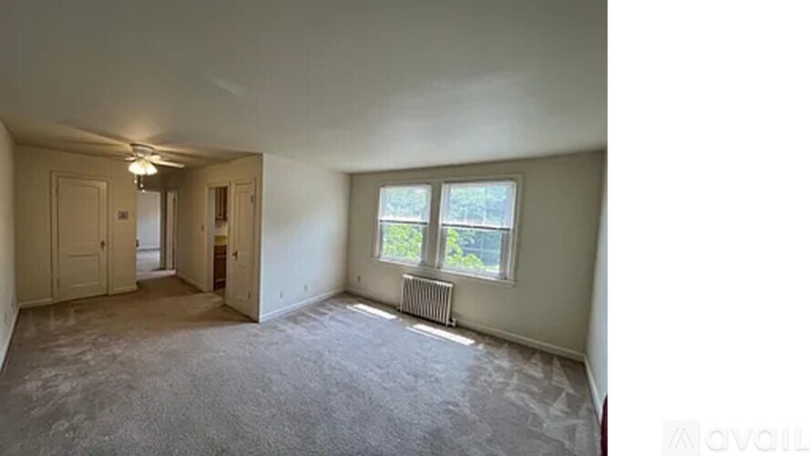 A room with a carpeted floor, a window with a view of trees, and a radiator.